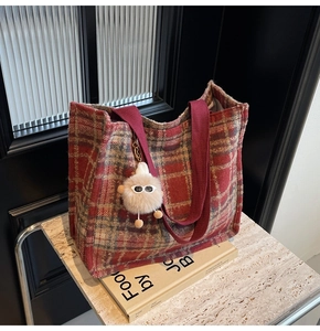 Detail of red-brown checkered wool tote bag with plush charm and woven shoulder strap