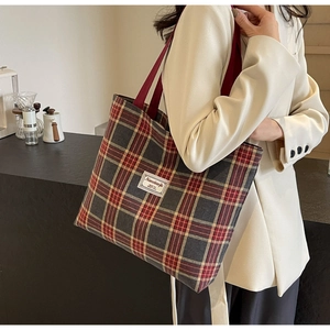 Detail of a vintage plaid canvas tote bag with red strap worn by a model in a cozy setting