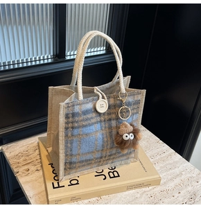 Detail of checkered linen tote bag with white rope handles and plush monster keychain