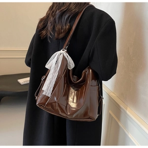 Détail d'un grand sac cabas marron foncé brillant orné d'un nœud en dentelle blanche
