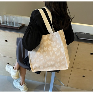Detail of beige canvas tote bag featuring 3D heart textures and wide shoulder straps