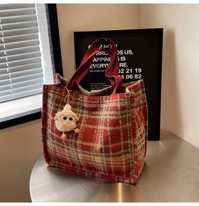 Close-up of red plaid tweed tote bag with fuzzy monster charm on a metal table