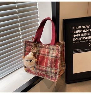 Detail of red plaid wool tote bag with plush charm and canvas handles on a windowsill