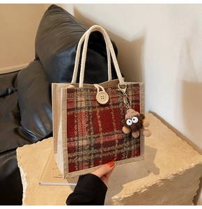 Close-up of red and green plaid jute tote bag with rope handles and a plush monster charm