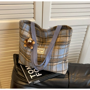 Détail d'un sac cabas en laine à carreaux bleus avec breloque peluche sur livre noir