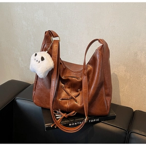 Détail d'un sac cabas marron avec lacets croisés et un pendentif panda en peluche