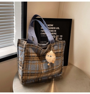 Close-up of wool plaid tote bag with blue straps and cute plush monster charm
