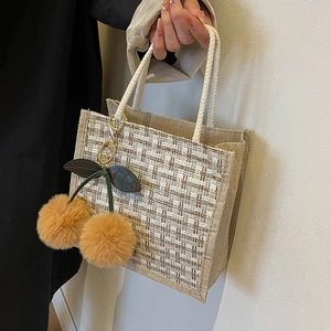 Linen woven tote bag with cherry charm and rope handle against a white wall background