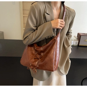 Détail d'un sac bandoulière en cuir PU marron avec laçage vintage porté par un mannequin