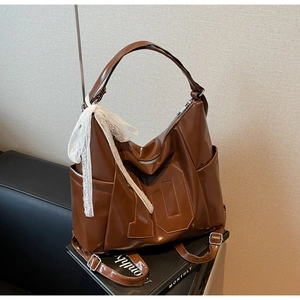 Détail du sac en similicuir marron brillant avec le numéro 10 et un foulard en dentelle