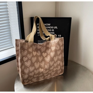 Detail of canvas tote bag with heart print and thick brown ribbon handles on a metal surface