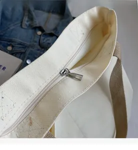 Close-up of thick beige canvas tote bag with smooth silver metal zipper closure