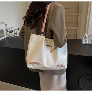 Detail of white tote bag with pink straps, heart charms, and decorative bows worn by model