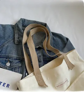 Detailed view of cream canvas tote bag with khaki straps and brand label on denim