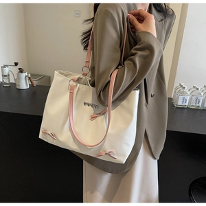 Detail of white tote bag with pink bows and heart charm worn by a model in a cafe