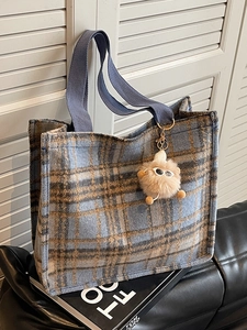 Blue and brown plaid wool tote bag with plush monster charm on a stylish leather sofa