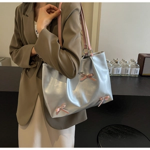 Detail of silver metallic tote bag featuring pink bow accents and shoulder straps for daily use
