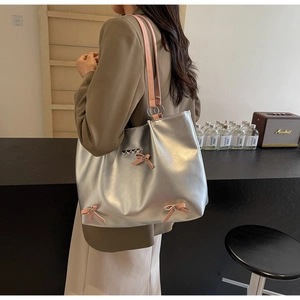 Detail of silver metallic tote bag with pink bow accents and leather shoulder straps