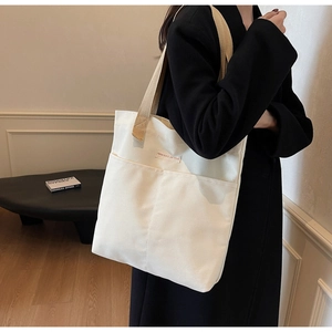 Detail of minimalist cream canvas tote bag featuring double front pockets and brown straps
