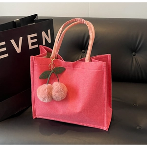 Detailed close-up of pink canvas tote bag with a cute cherry plush charm on dark sofa