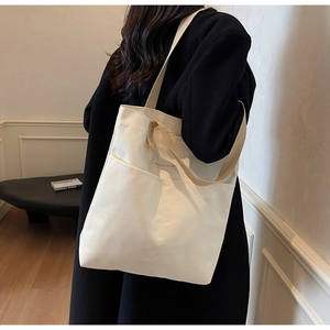 Detail of minimalist cream canvas tote bag showing the front pocket and brand label