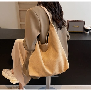 Lifestyle view of a large camel suede tote bag worn by a model in a cozy cafe setting