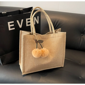 Close-up of linen tote bag featuring a cute plush cherry charm on a black leather sofa