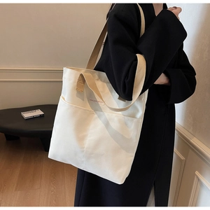 Detail view of the white canvas tote bag featuring double front pockets and red brand label