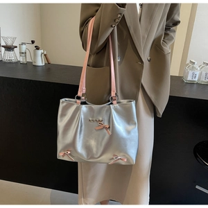 Detail of silver tote bag with pink bow accents and heart charms in a cafe setting