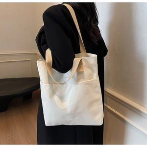 Close-up of off-white canvas tote bag with khaki handles and front pocket detail