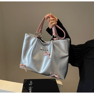 Detail of silver tote bag featuring pink bow and heart charm with polished metallic finish