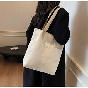 Detailed side view of off-white canvas tote bag with woven straps and front pocket