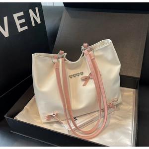 Detail of a large cream tote bag with pink bows and heart buckles inside a black gift box