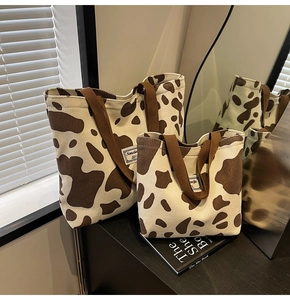 Détail de grands et petits sacs cabas en velours à motif vache sur un meuble sombre