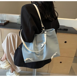 Detailed view of light blue tote bag with white bow and heart charm on a shoulder strap