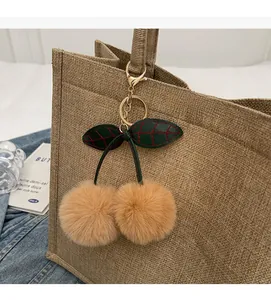 Detailed view of plush cherry bag charm with brown pom poms and golden metal clasp