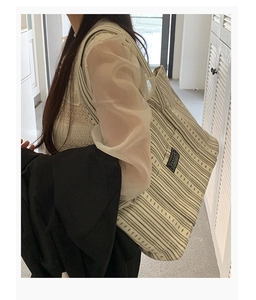 Detail view of large striped canvas tote bag with fashion label and thick shoulder strap