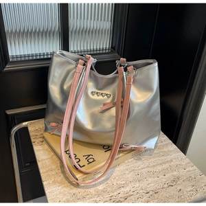 Detail of silver tote bag with pink bow accents and heart rivets on marble surface