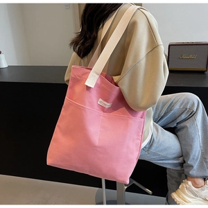 Detail of pink canvas tote bag with dual straps and front pockets on a model