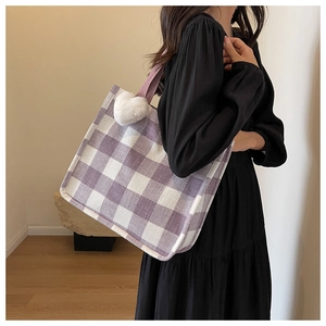 Detail of purple plaid tote bag with soft white heart plush charm on a woven strap