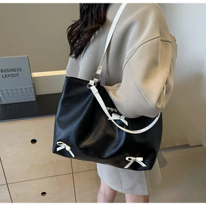 Detail view of black leather tote bag with white bow and rhinestone accents