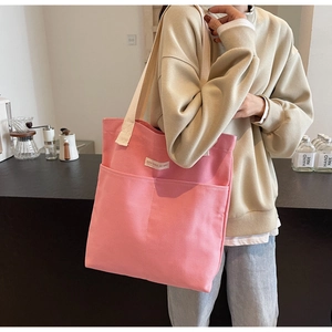 Detailed side view of pink canvas tote bag with dual front pockets and cream straps