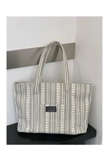 Detail view of large striped canvas tote bag with fashion label and thick shoulder straps