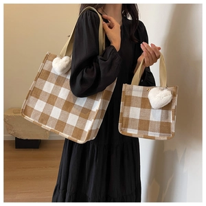 Detail of plaid tote bag set with heart charm and khaki straps on a dark dress