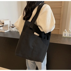 Detailed view of black canvas tote bag with outer pocket and brand tag in cafe setting