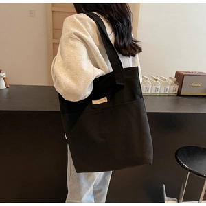 Detail of a black large-capacity canvas tote bag featuring an external pocket and side label