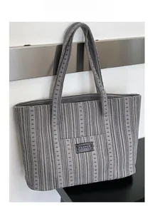 Close-up detail of grey striped tote bag showing textured fabric and fashion logo patch