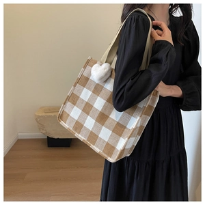 Detail of checkered tote bag with woven texture, heart plush charm, and thick strap