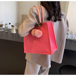 Rear view of a bright pink linen tote bag with plush cherry charm on a female model