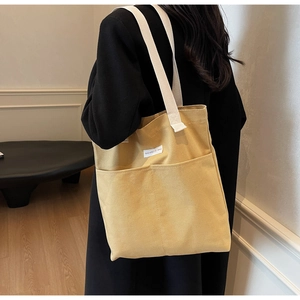 Detailed side view of yellow canvas tote bag with two front pockets and woven straps